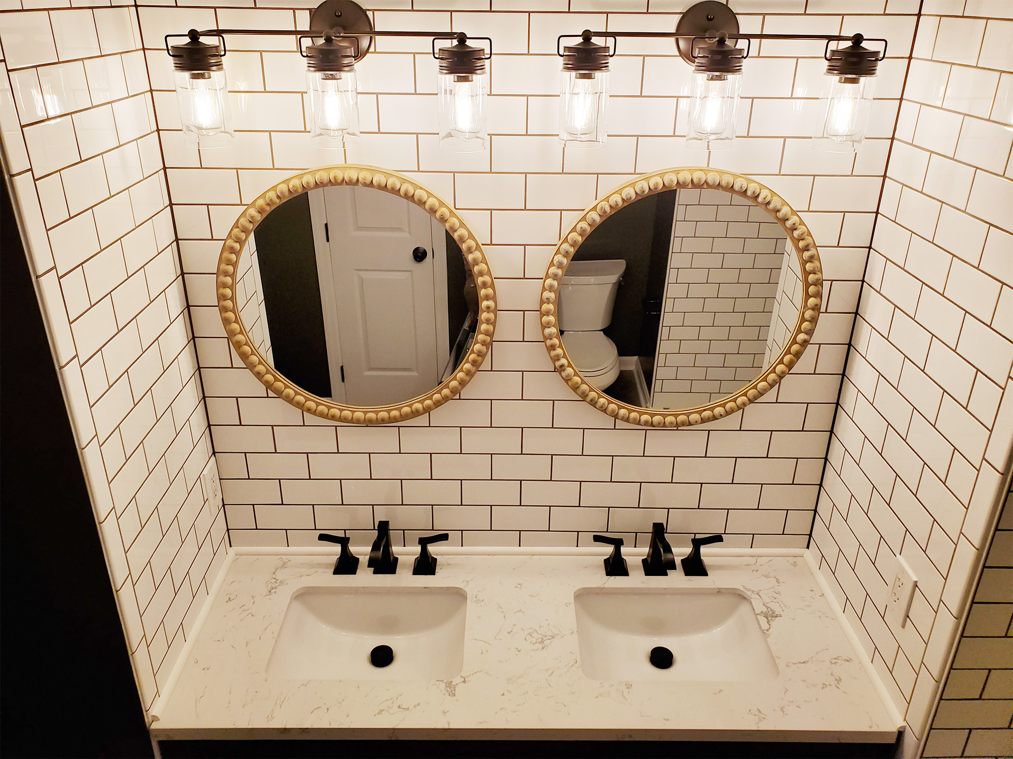 A two sink vanity with new lighting, mirrors, and tile